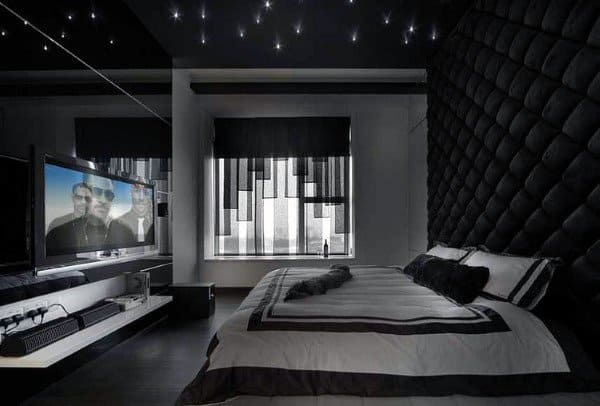 Modern black bedroom with tufted walls, starry ceiling lights, and a large TV setup.