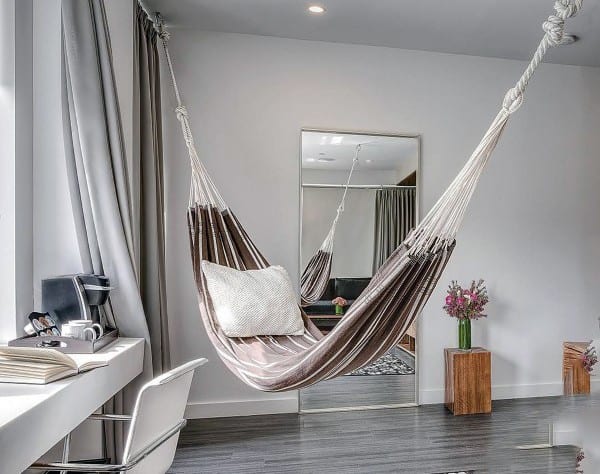 Indoor hammock with a cozy pillow in a modern bedroom featuring a desk and large mirror.