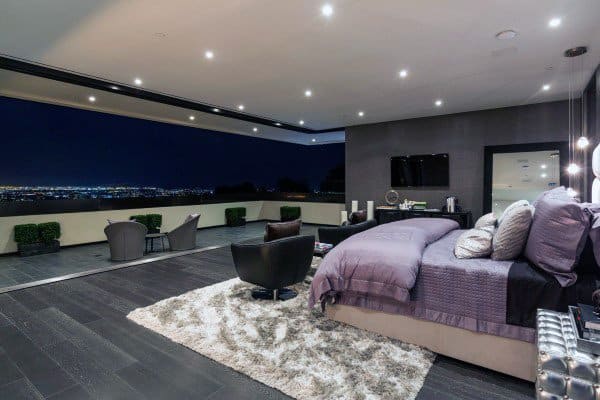 Spacious modern bedroom with city view, outdoor seating, and plush purple bedding.
