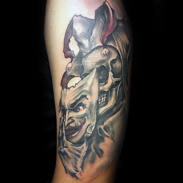A vibrant tattoo of a jester's face transforming into a skull, with a detailed jester hat, showcasing a blend of playful and eerie elements.