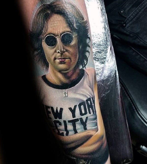Hyper-realistic color tattoo of John Lennon wearing his iconic "New York City" shirt and round sunglasses, with lifelike detail and shading.