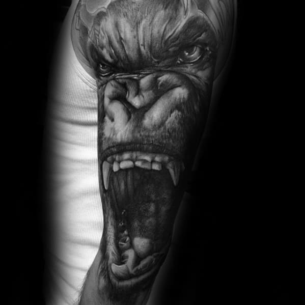 Hyper-realistic King Kong tattoo on upper arm showing an intense close-up of Kong roaring with a woman inside his open mouth.