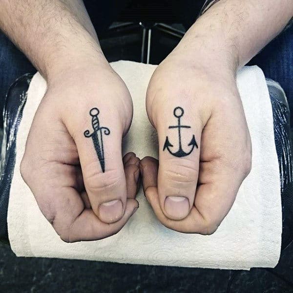 Two hands showing tattoos: a dagger on the left thumb and an anchor on the right thumb