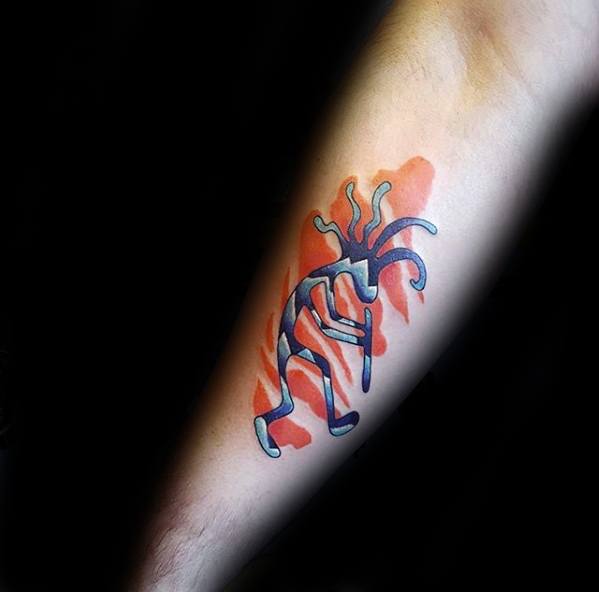 Stylized Kokopelli tattoo in blue shades with curved limbs, set against a bold red watercolor-style background on the forearm.