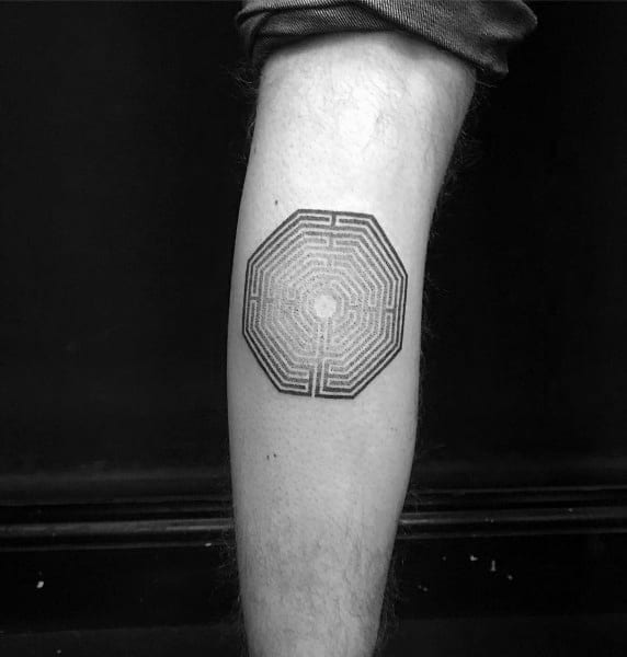 Octagonal labyrinth tattoo on a man's calf, featuring intricate maze-like lines leading to a small central point in fine black ink.