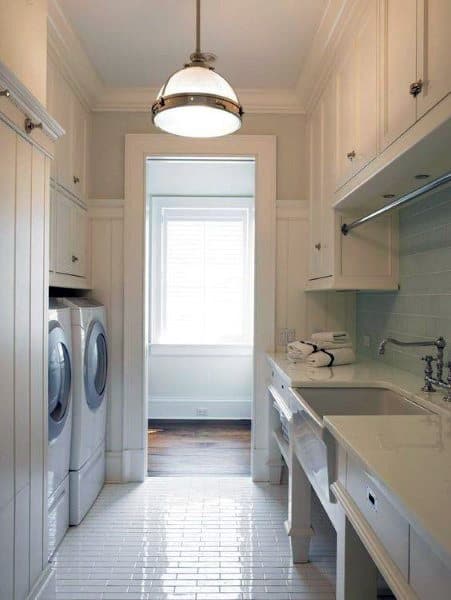 Narrow laundry room with white cabinets, tile flooring, modern appliances, and soft natural light.