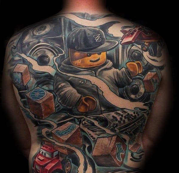 Full back tattoo of a Lego DJ figure wearing a cap, surrounded by speakers, blocks, a turntable, and animated graffiti-style elements.