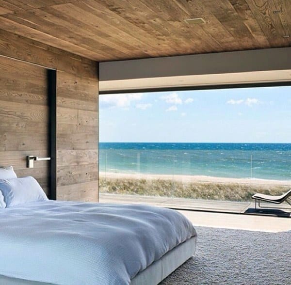 Luxurious bedroom with wood accents and a stunning ocean view through floor-to-ceiling windows.