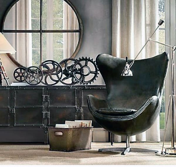 A modern interior with a black swivel chair, metal gears decor, a round mirror, and a floor lamp