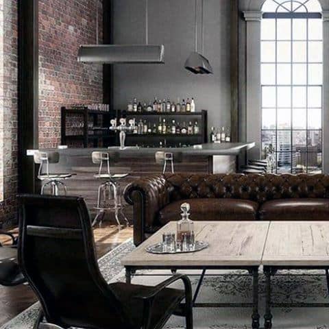Loft-style living room with a leather sofa, wooden coffee table, bar area, brick walls, and large windows