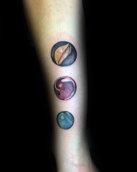 Colorful marble tattoo design on the forearm, featuring three realistic marbles with detailed shading and reflections for a bold look.