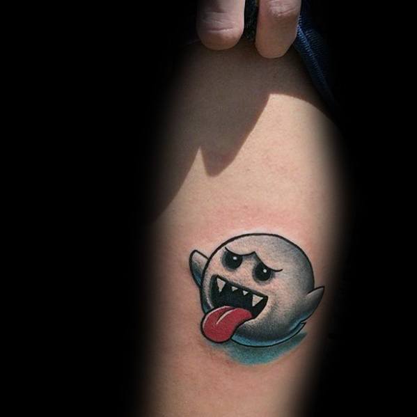 Mario ghost tattoo featuring Boo with a playful expression, sticking out its tongue, shaded in black and blue, inked on the upper arm.