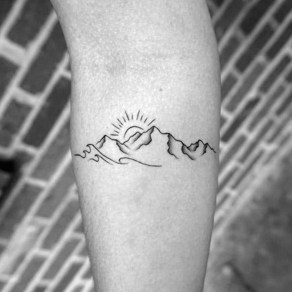 Minimalist mountain tattoo on the forearm, featuring a rising sun with rays and simple wave-like lines for a nature-inspired design.