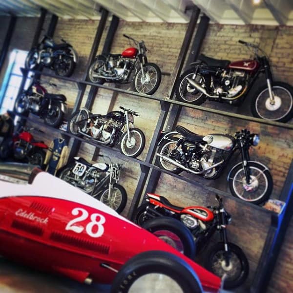 A stunning dream garage featuring a motorcycle wall rack paired with a vintage race car centerpiece.