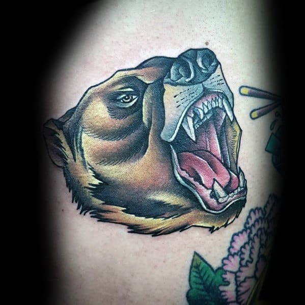 Neo-traditional bear tattoo with bold shading, open jaws, and fierce expression, complemented by floral and decorative elements.