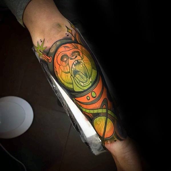 Neo-traditional gorilla tattoo in a space suit with bold orange and green tones, screaming expression, and cosmic background.