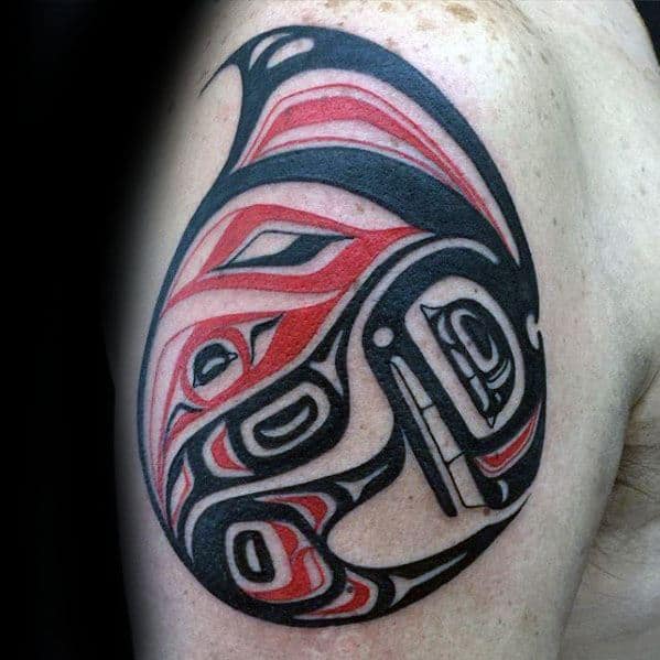 Bold black and red orca tattoo on the upper arm, featuring intricate tribal-inspired patterns with smooth curves and sharp angles for a striking visual effect.