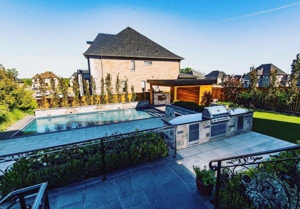 Modern outdoor backyard with pool, patio, built-in grill, and a brick house