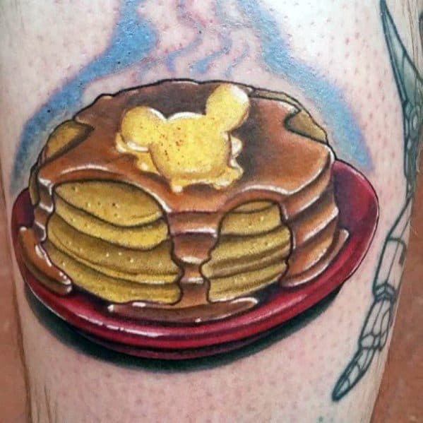 Pancake tattoo with syrup and Mickey-shaped butter on a red plate, featuring bold shading and a realistic style for a playful touch.