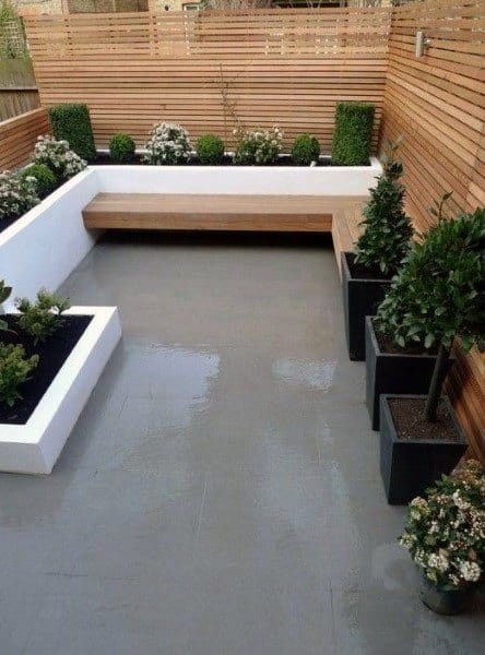 Minimalist patio with a wooden bench, lush potted plants, and gray flooring, all surrounded by elegant wooden fencing