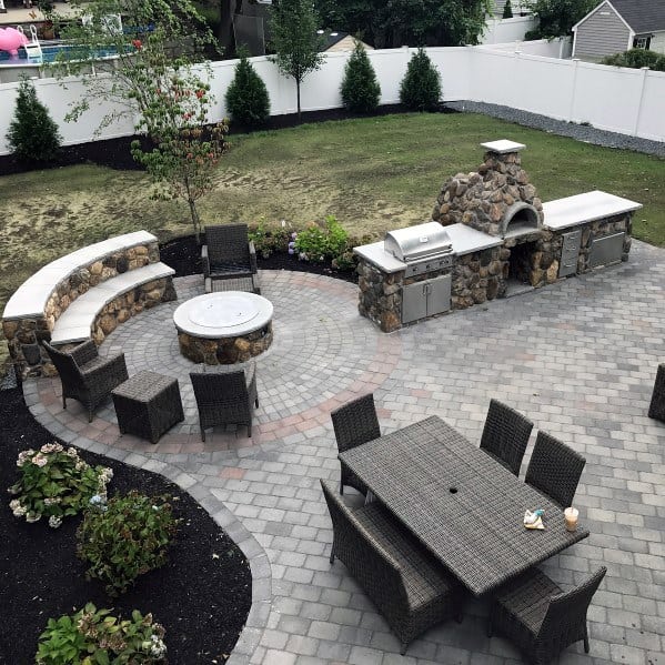Backyard with a stone patio featuring a built-in grill, pizza oven, fire pit, and outdoor furniture