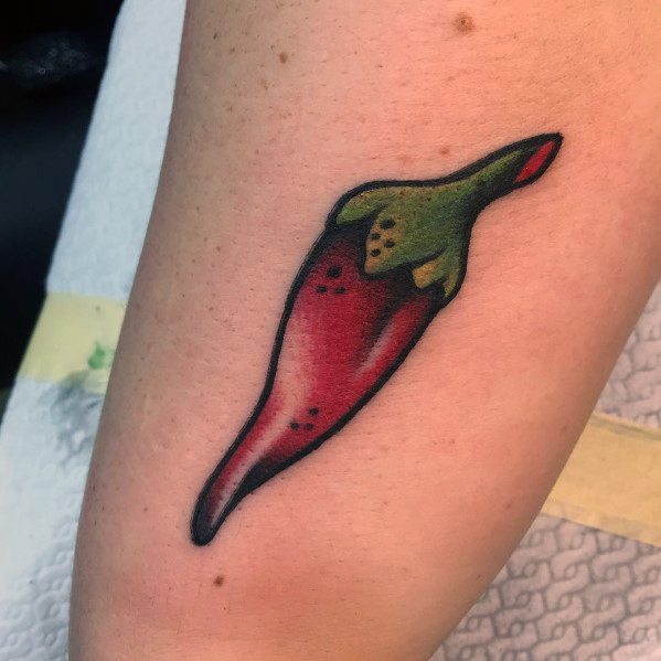 Vibrant red and green chili pepper tattoo on the arm with bold shading and a black outline for a striking, classic look.