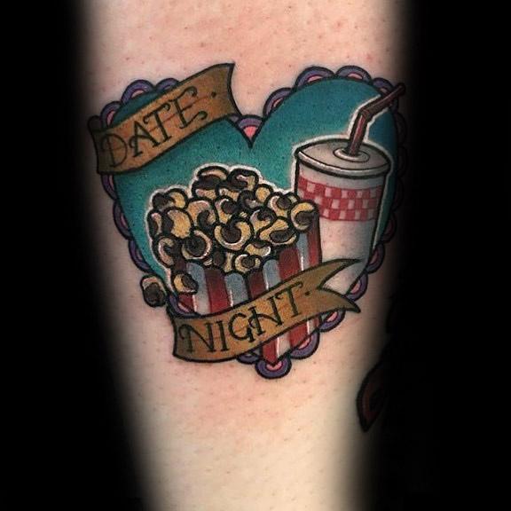 Tattoo of a heart-shaped frame with popcorn, a soda cup, and banners reading DATE NIGHT in a retro style.