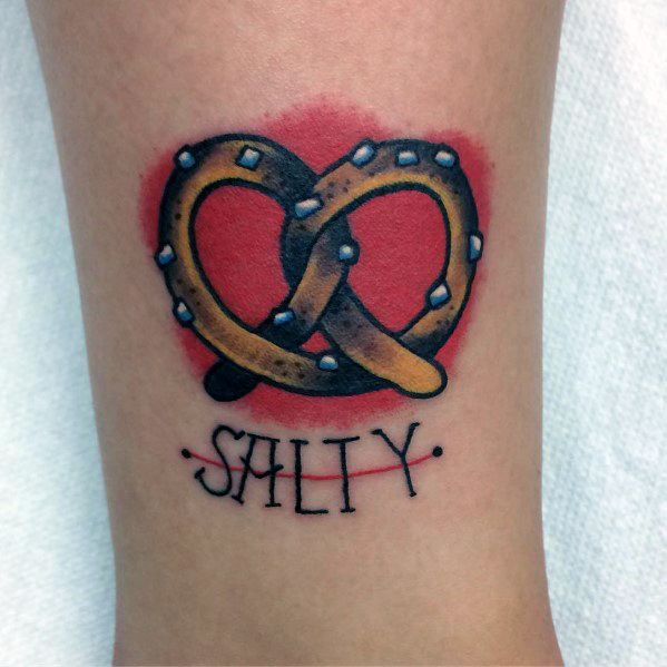 Golden pretzel tattoo with salt details and a red background, featuring the word "SALTY" in bold black lettering underneath.