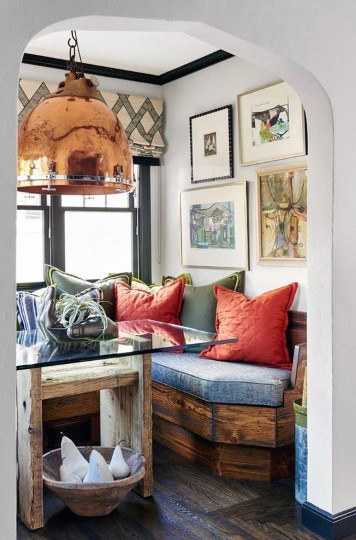 Cozy nook with a wooden bench, vibrant cushions, glass table, copper pendant light, and framed art on the walls