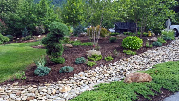 Beautiful river rock landscaping with various plants, trees, and rocks creating a natural, textured garden design