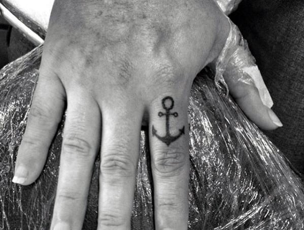 Small black anchor tattoo on the finger, featuring a minimalist design that symbolizes strength, stability, and a deep nautical connection.