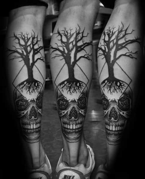 Matching calf tattoos of a tree with exposed roots growing from a detailed skull, framed by a diamond shape for a bold symmetrical look.