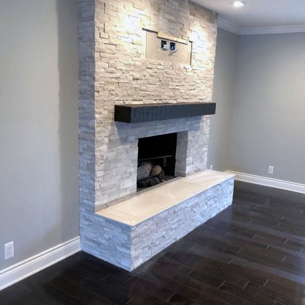 Modern stacked stone fireplace with sleek black mantel and white hearth in a cozy living room