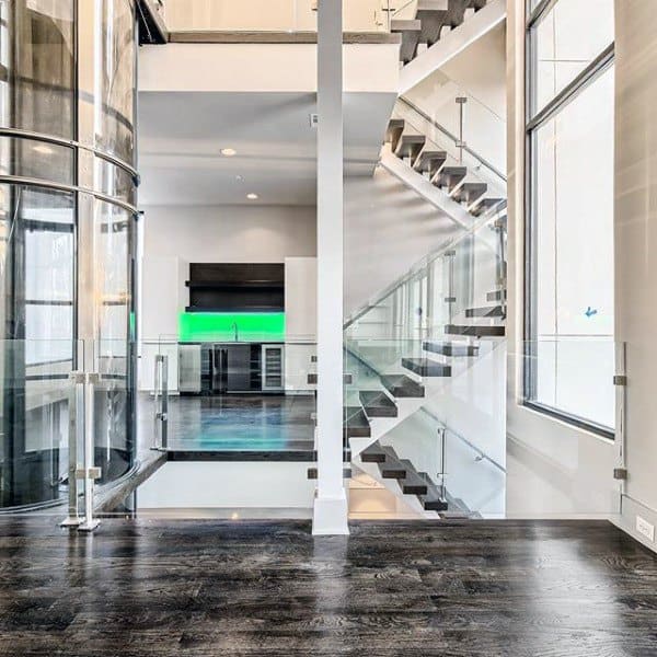 Modern interior with a sleek staircase, dark wood floors, and a kitchen featuring a green-lit backsplash