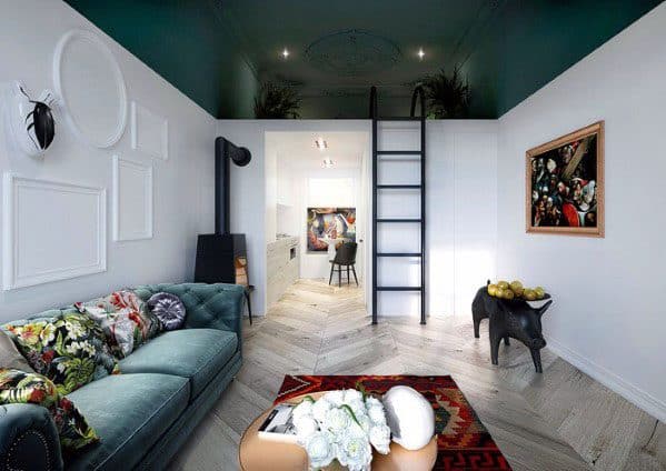 Elegant studio with loft bed, green sofa, floral accents, ladder, and herringbone flooring.
