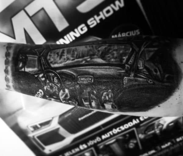 Black and grey Subaru-themed tattoo depicting a detailed rally car interior view, showcasing the dashboard, roll cage, and racing elements.