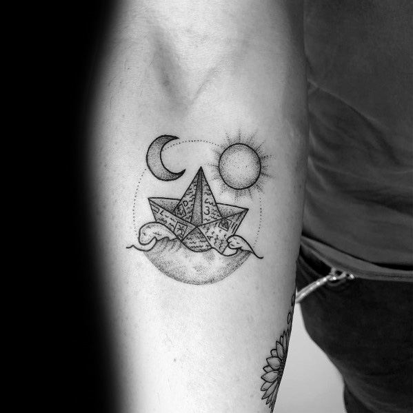 Intricate paper boat tattoo with waves, sun, and moon, symbolizing balance, exploration, and the passage of time.