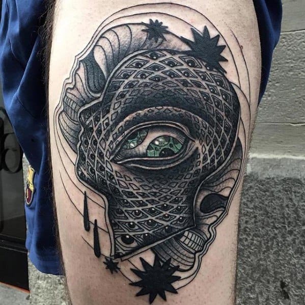 Black and grey Tool-inspired tattoo with an intricate patterned face, central green eye, and surreal cosmic elements on the thigh.