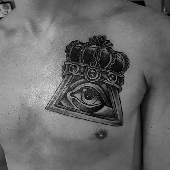 Black and grey chest tattoo of the all-seeing eye inside a triangle, topped with a detailed royal crown in a bold style.