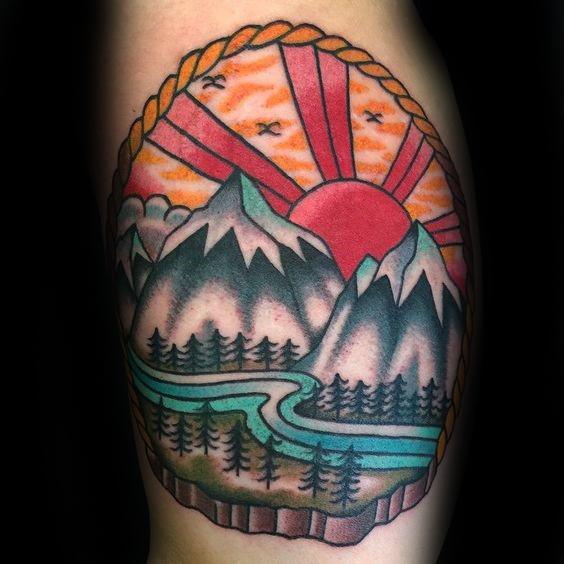 Bold mountain landscape tattoo with a winding river, tall pines, and a vivid red sunrise framed by a rope border.