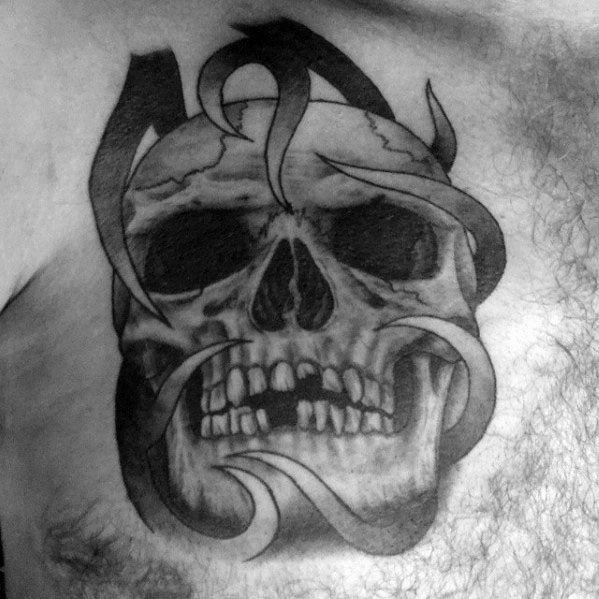 Realistic skull tattoo on the chest with bold tribal-style flames wrapping around and through the skull in dark black ink.