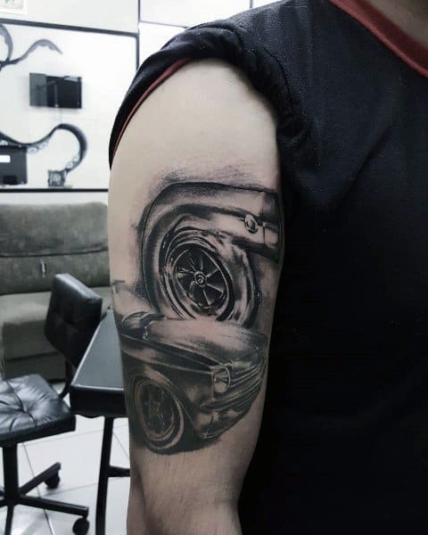 Realistic automotive-themed tattoo on the upper arm featuring a detailed turbocharger and classic muscle car, symbolizing speed, power, and passion for cars.