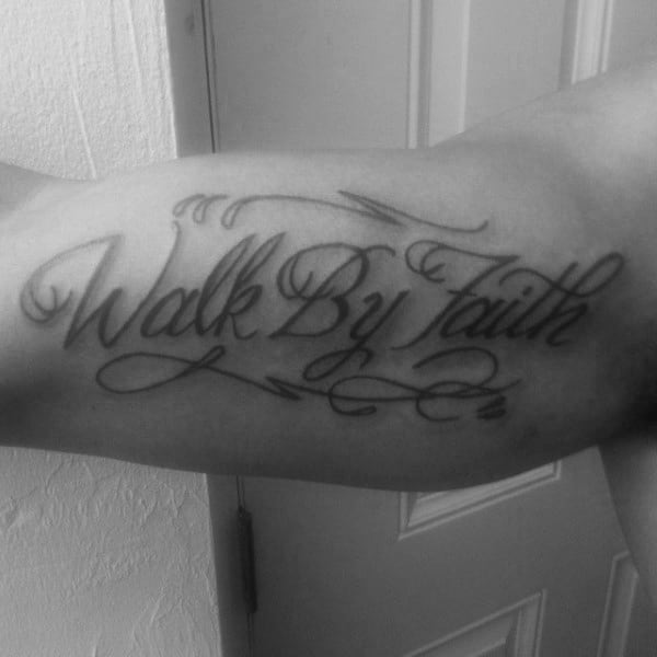 Bicep tattoo featuring "Walk By Faith" in elegant cursive script with decorative flourishes, symbolizing strength and spiritual belief.