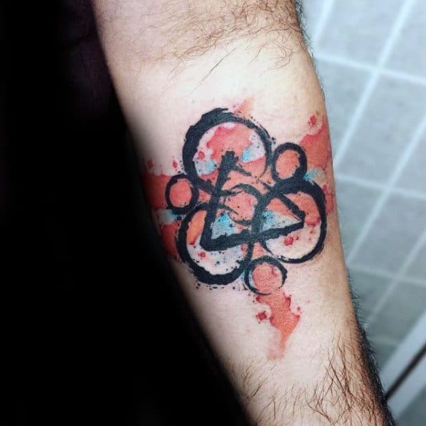 Coheed and Cambria Keywork tattoo with watercolor red and blue splashes, blending grunge and abstract art styles on the forearm.