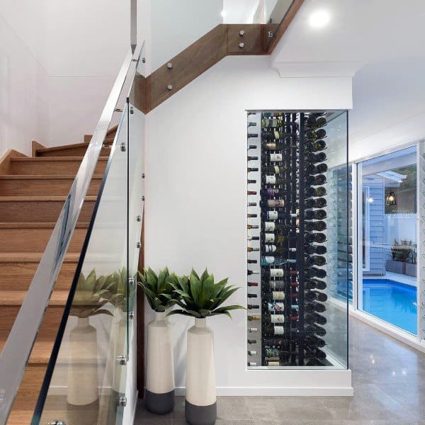 Modern staircase with glass railing, wine rack, large windows, and potted plants beside a pool view