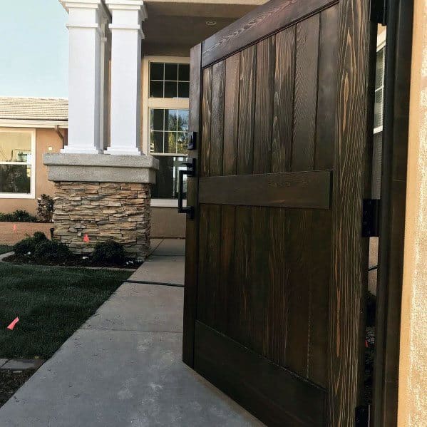 Tall wooden gate opening to a modern house entrance