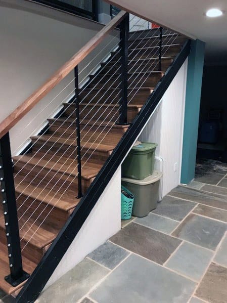 Modern wooden staircase with cable railing and storage bins underneath in a basement.