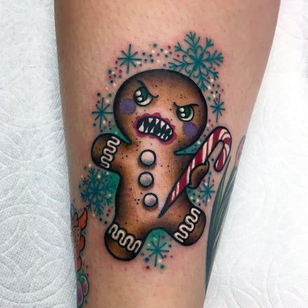 Christmas tattoo of an angry gingerbread man holding a candy cane, surrounded by snowflakes, with a fierce expression and battle-ready stance.
