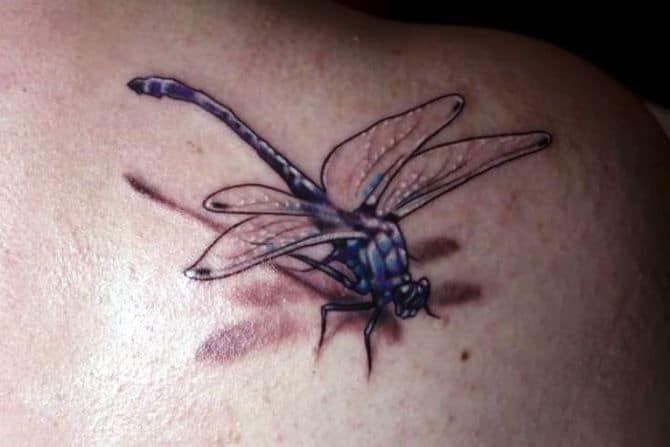 Realistic 3D dragonfly tattoo with translucent wings and a shadow effect, placed on the upper back or shoulder.