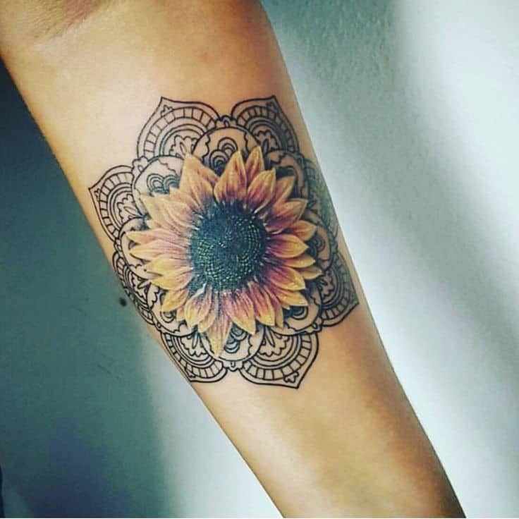 Colorful sunflower tattoo on forearm with warm yellow and orange petals, framed by an intricate black mandala design.